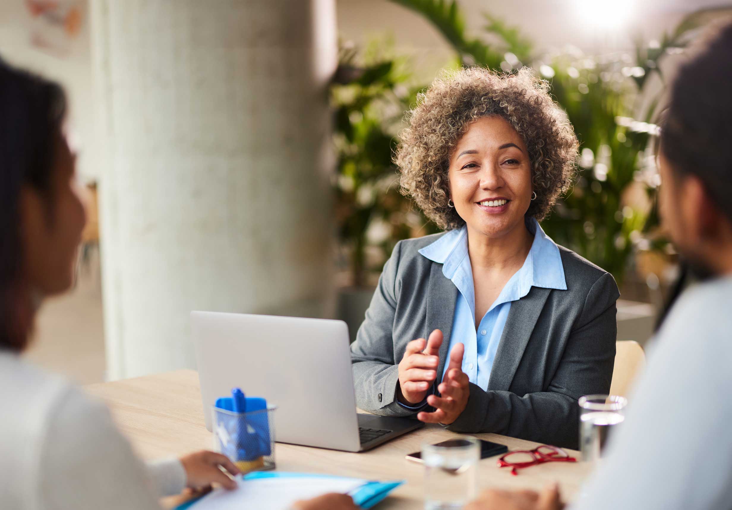 A Stravon Offshore Bank financial advisor with short curly hair is smiling and gesturing while seated at a table with her computer. She is meeting with a client to discuss their financial needs, symbolizing the expert and personalized service we offer.